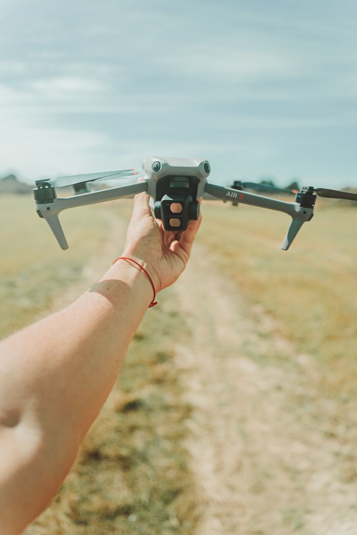 gallery-4 Person gripping a DJI drone in a sunny open field, ready for takeoff or landing.